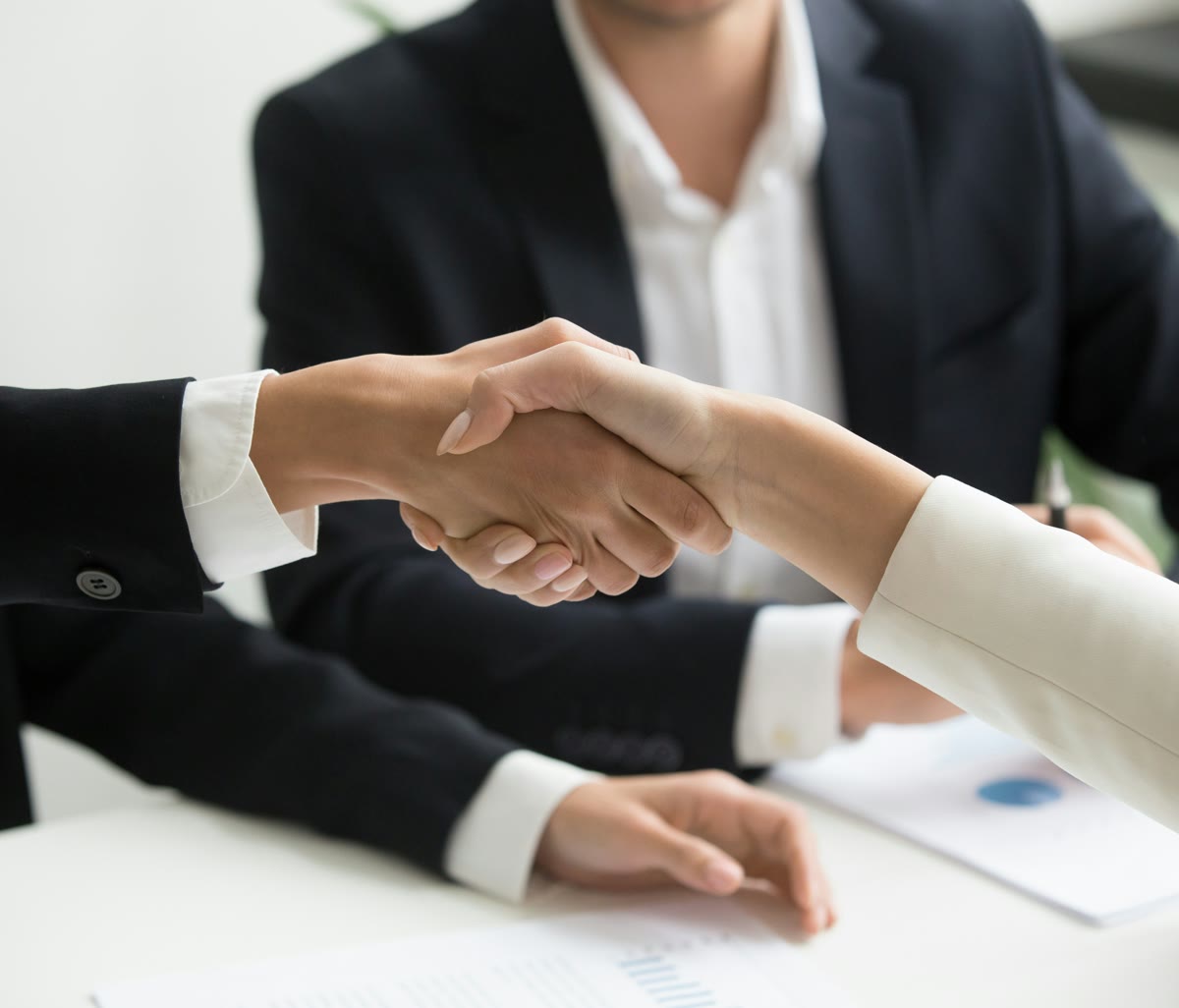 Advisors shaking hands across a conference table during a transaction meeting